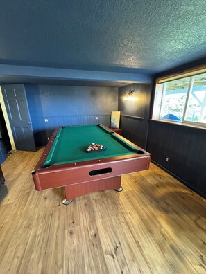 Een pooltafel met een groen vilt oppervlak, omringd door houten vloer en donkerblauwe wanden.