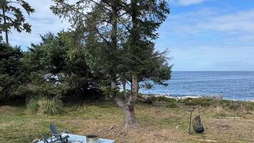 Een houten terras met tuinmeubilair, uitzicht op de oceaan en een boom.