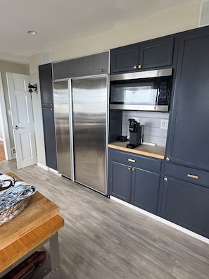 A modern kitchen with stainless steel appliances, dark cabinetry, and a wooden dining table.