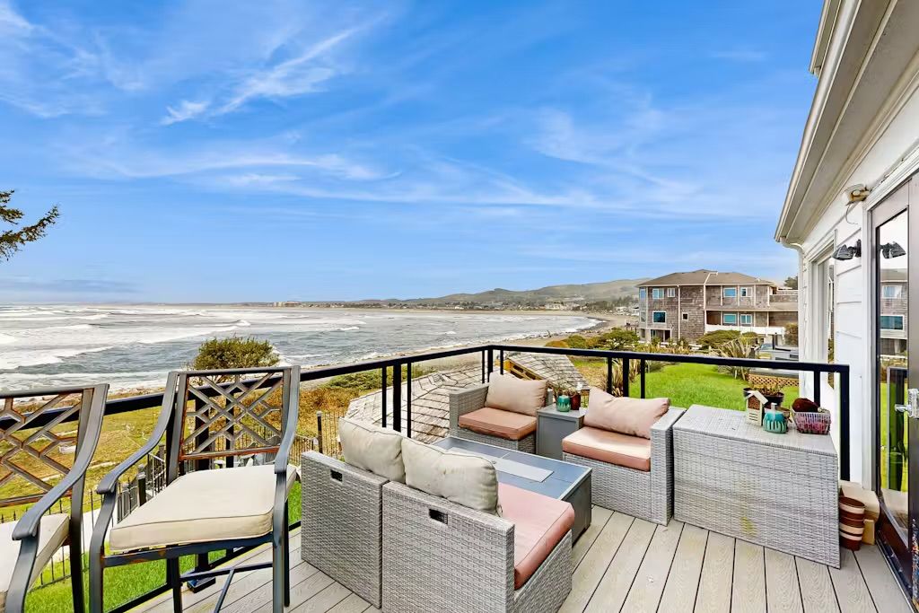 Un balcon doté de meubles en osier, offrant une vue sur une plage et l’océan.
