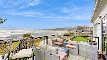 A balcony with wicker furniture overlooking a beach and ocean.