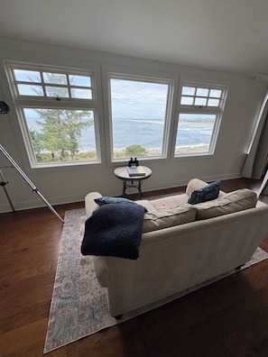 A room with a sofa, a small table, and a view of the sea through large windows.