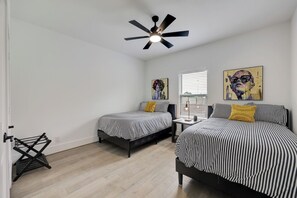 Ein Schlafzimmer mit zwei Betten, einem Deckenventilator, einem Fenster mit Jalousien und Bildern an den Wänden.