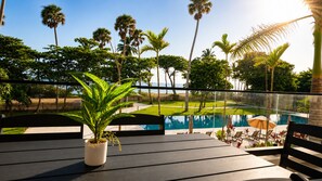 Un espace aménagé au bord de la piscine, offrant une vue sur la piscine, les palmiers et une plante en pot sur une terrasse en bois.