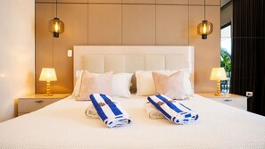 Une chambre d’hôtel avec un grand lit, deux tables de chevet, une lampe et deux serviettes sur lesquelles figure le nom de l’hôtel.