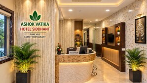 A hotel reception area with a marble reception desk, a reception sign, and potted plants. - Ashok Vatika Hotel Siddhant (Indore)