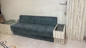 A room with a grey sofa, two side tables, a wall-mounted power outlet, and a framed collage on the wall. - Ashok Vatika Hotel Siddhant (Indore)