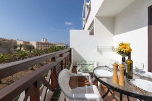A balcony with a wooden railing, white plastic chairs, a round table set with plates, glasses, and a vase with yellow flowers. - Victoria Court II H116 - One Bed (Los Cristianos)
