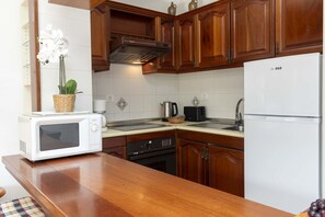A kitchen with wooden cabinets, a white refrigerator, a microwave, a stove, and a sink. - Victoria Court II H116 - One Bed (Los Cristianos)