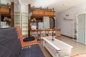 A modern living room with a sofa, dining table, chairs, and a kitchen area. - Victoria Court II H116 - One Bed (Los Cristianos)