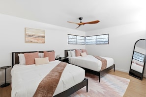 Une chambre avec deux lits, un ventilateur de plafond, un tableau et un grand miroir.