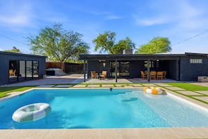 Un espace piscine extérieur moderne, doté d’une piscine à l’eau d’un bleu limpide, d’un flotteur circulaire et d’un coin salon abrité avec des chaises.