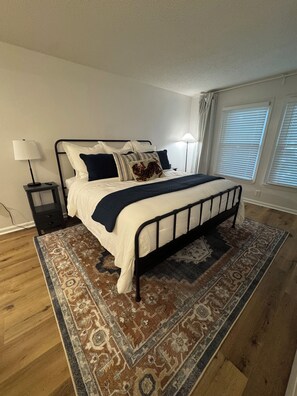 Un dormitorio con cama, dos mesitas de noche, una alfombra y una ventana con persianas.