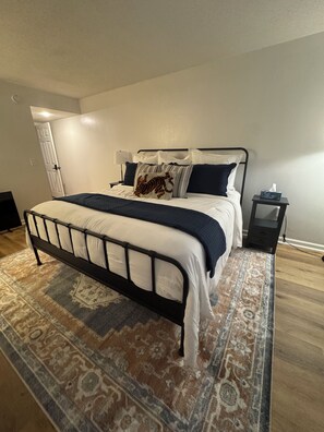 Un dormitorio con cama, mesita de noche, alfombra y puerta.