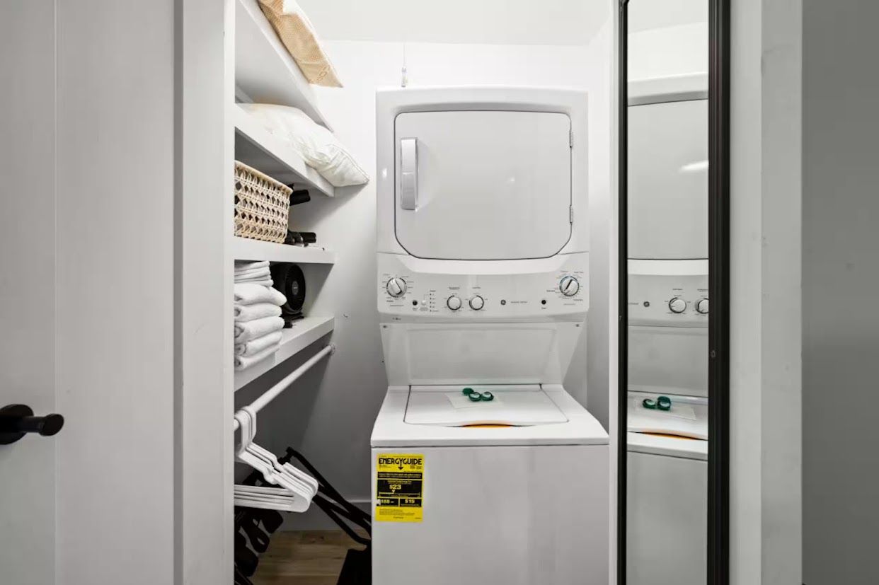 Une petite buanderie comprenant un lave-linge, des étagères avec des serviettes pliées et un panier.