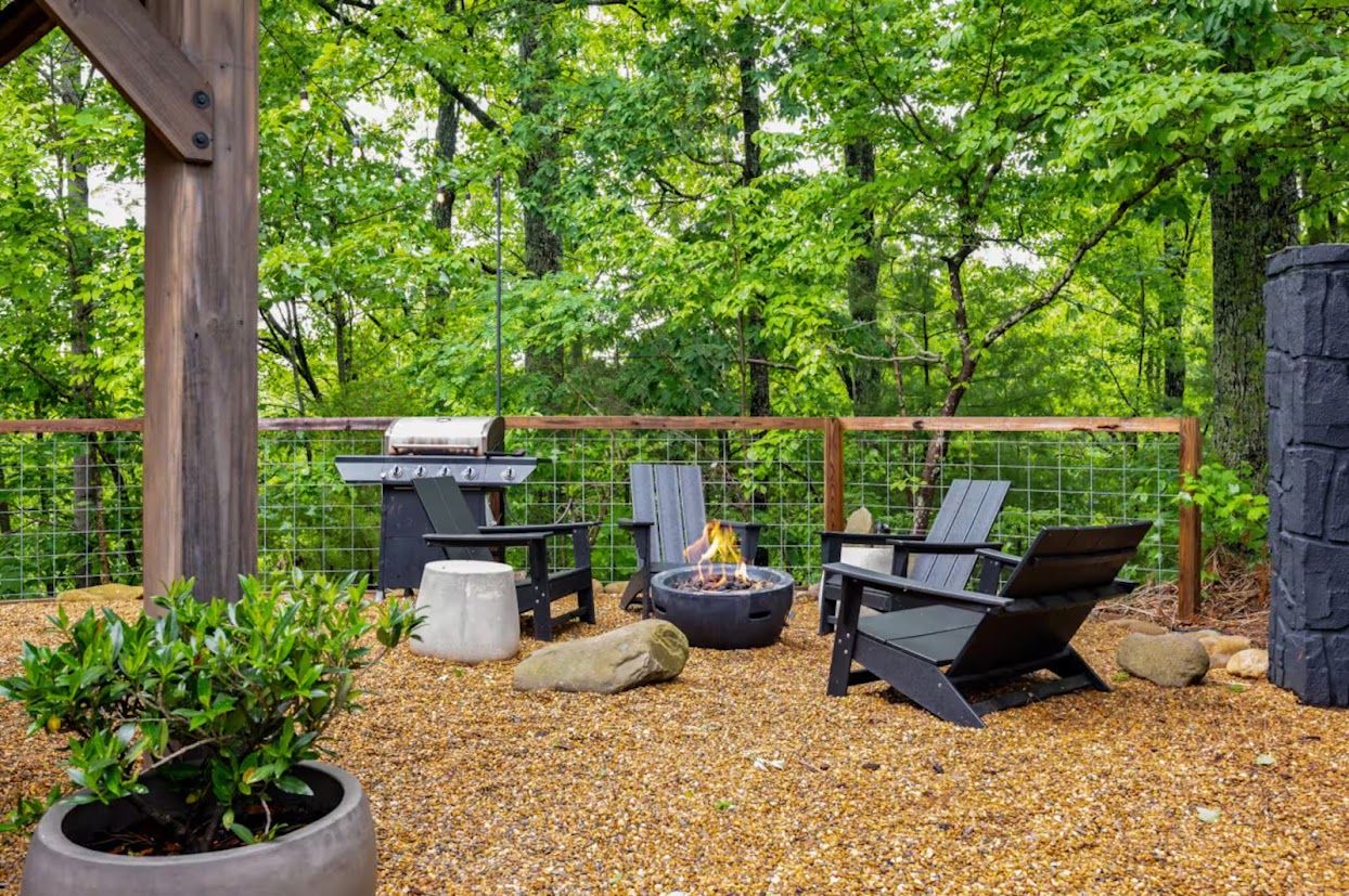 Une terrasse extérieure équipée d’un barbecue, d’un foyer et d’un espace salon, le tout entouré d’une clôture et d’arbres.