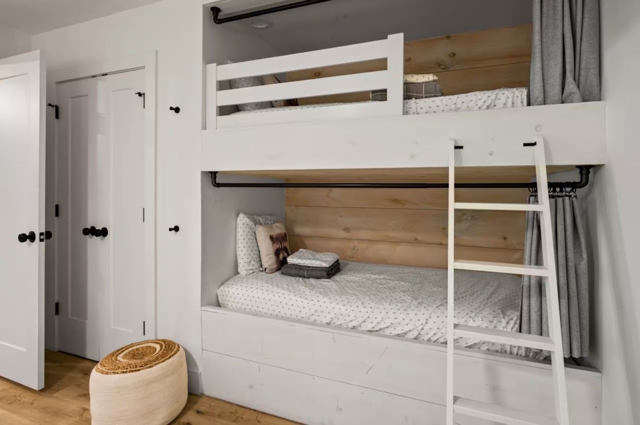 Un lit superposé avec une échelle, une porte avec une poignée et un pouf en osier tressé.