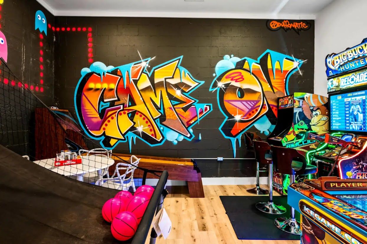 Une salle d’arcade avec des murs décorés de graffitis colorés, différents jeux d’arcade et un panier de basket.