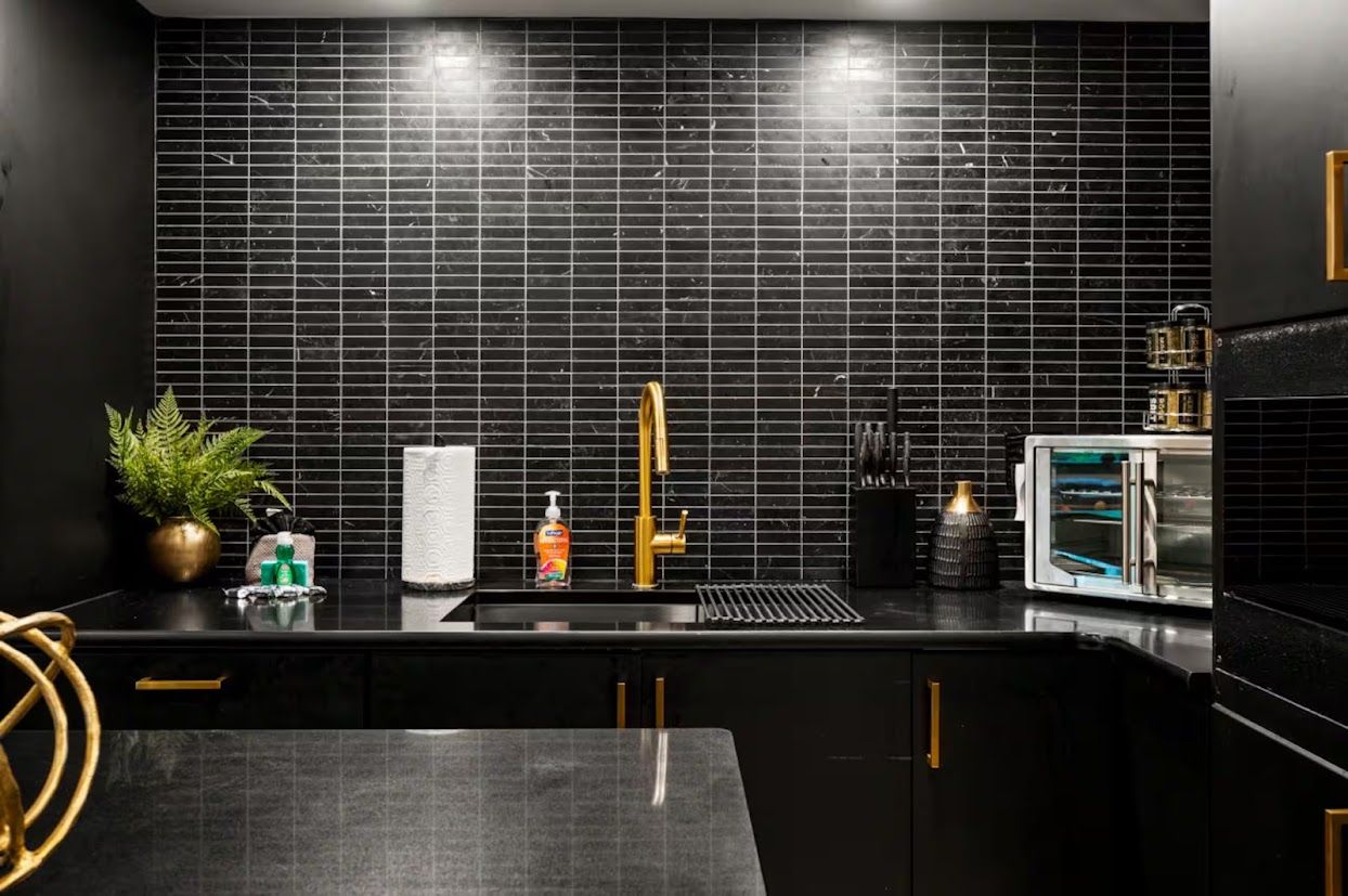 A modern kitchen with black tiles, a gold faucet, and a built-in oven.