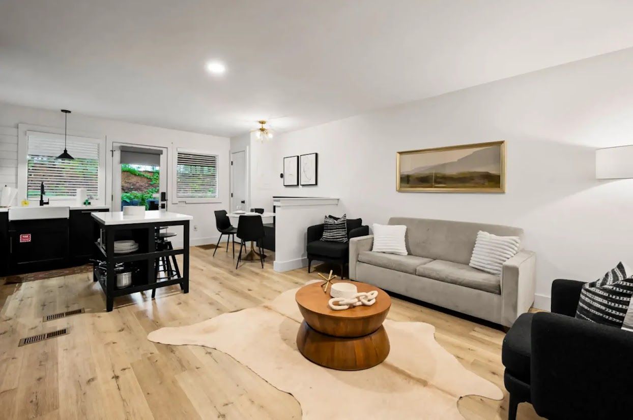 A modern living room with a grey sofa, a round wooden coffee table, and a dining area with a black table and chairs.