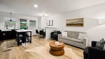 A modern living room with a grey sofa, a round wooden coffee table, and a dining area with a black table and chairs.
