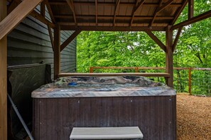 A hot tub under a wooden pergola with a view of trees.