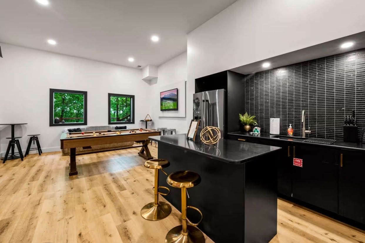 A modern kitchen with a central island, bar stools, a foosball table, and a large refrigerator.