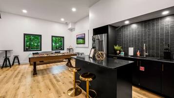 A modern kitchen with a central island, bar stools, a foosball table, and a large refrigerator.