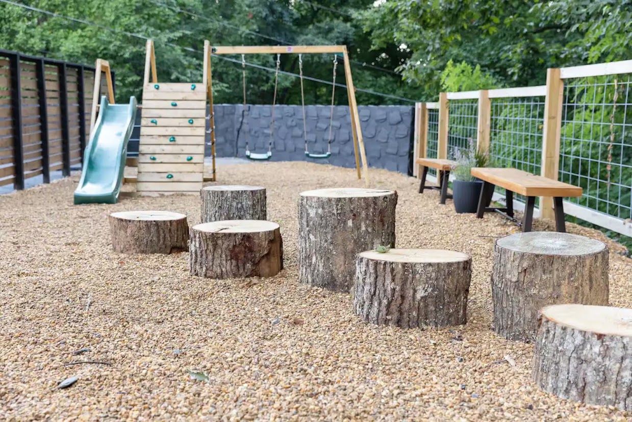 Ein Spielplatz mit Rutsche, Schaukeln und Baumstümpfen.
