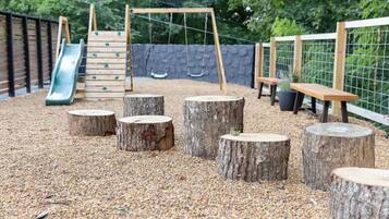 Ein Spielplatz mit Rutsche, Schaukeln und Baumstümpfen.