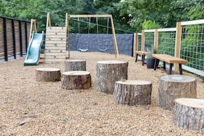 Un parque infantil con un tobogán, columpios y troncos de madera.