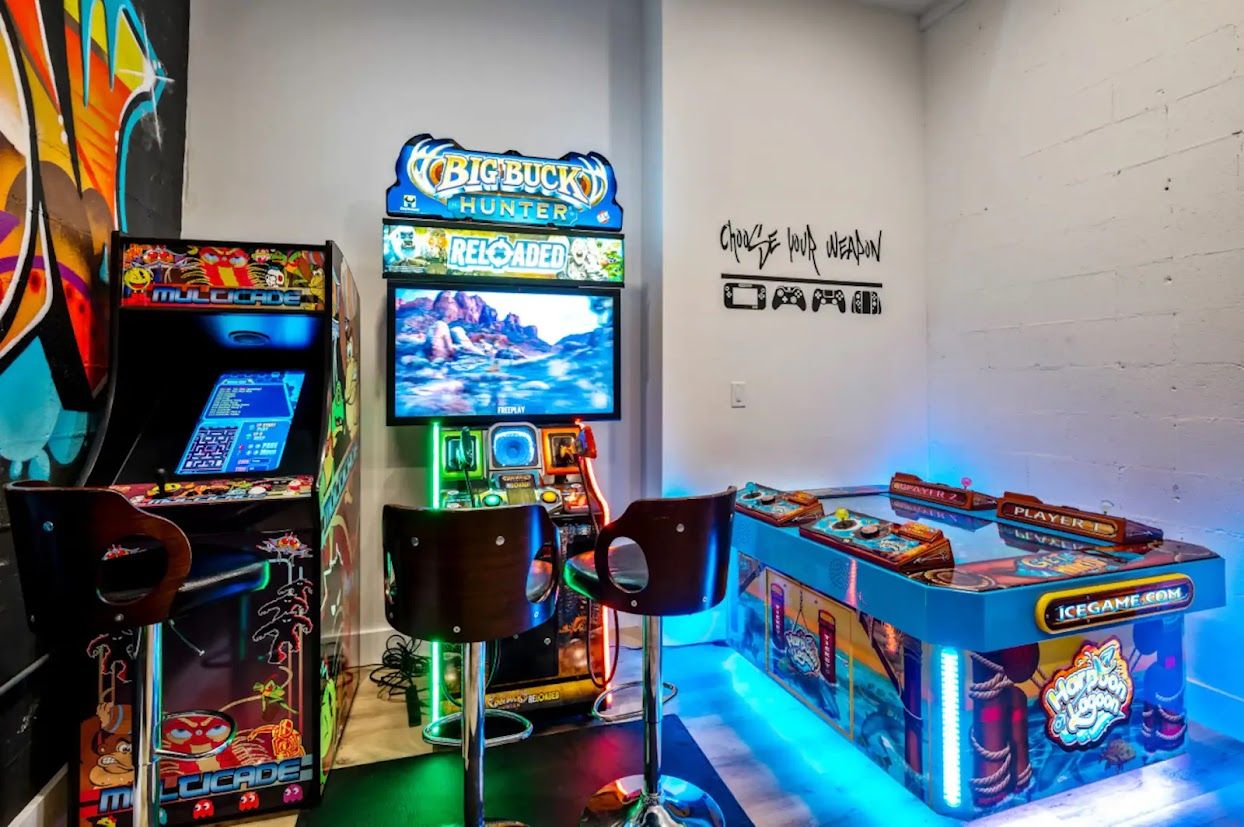 Ein Raum mit Spielautomaten, darunter ein 'Big Buck Hunter'-Spiel, und einer Wand mit Graffiti-Kunst.