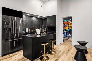 Una cocina moderna con una isla negra, electrodomésticos de acero inoxidable y taburetes dorados.