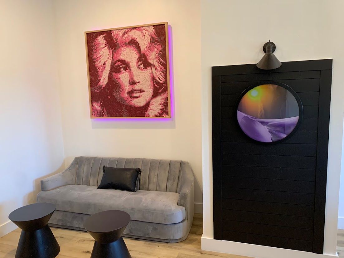 Un salon avec un canapé gris, deux tables d’appoint noires, une œuvre d’art encadrée et un miroir rond sur un mur noir.