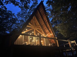 Una cabaña de madera con techo triangular y ventanas grandes, rodeada de árboles.