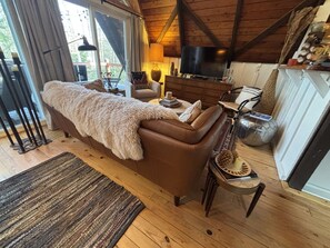 Una sala acogedora con un sofá de cuero, un televisor y un techo de madera rústica.