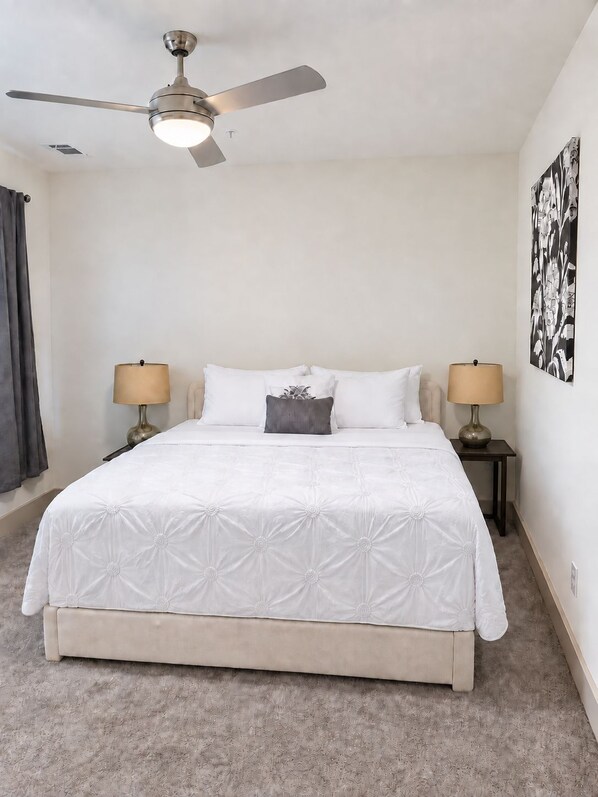 Un dormitorio con cama, dos lámparas de noche, ventilador de techo y una obra de arte en la pared.