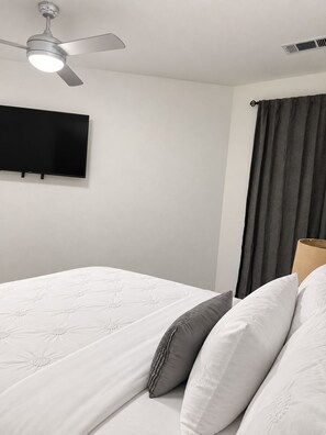 Een hotelkamer met een bed, een plafondventilator, een flatscreen televisie aan de muur en een raam met gordijnen.