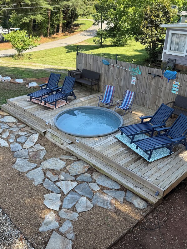 A backyard with a hot tub surrounded by lounge chairs, a wooden deck, and a stone pathway. - Cozy 2-bedroom apartment with AC in charming Mooresville (MOORESVILLE)