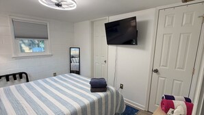 Une chambre à coucher avec un lit, un téléviseur fixé au mur, une fenêtre avec des stores et une porte.