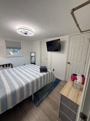 A bedroom with a bed, a television mounted on the wall, a window with blinds, and a door. - Cozy 2-bedroom apartment with AC in charming Mooresville (MOORESVILLE)