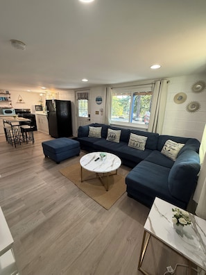 A modern living room with a sectional sofa, a round coffee table, and a kitchen area with a refrigerator and microwave. - Flip-Flop down to the Lake; Cozy 2-bedroom apartment with AC (MOORESVILLE)
