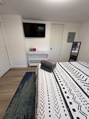 A bedroom with a bed, a TV mounted on the wall, a white door, and a small white cabinet. - Flip-Flop down to the Lake; Cozy 2-bedroom apartment with AC (MOORESVILLE)
