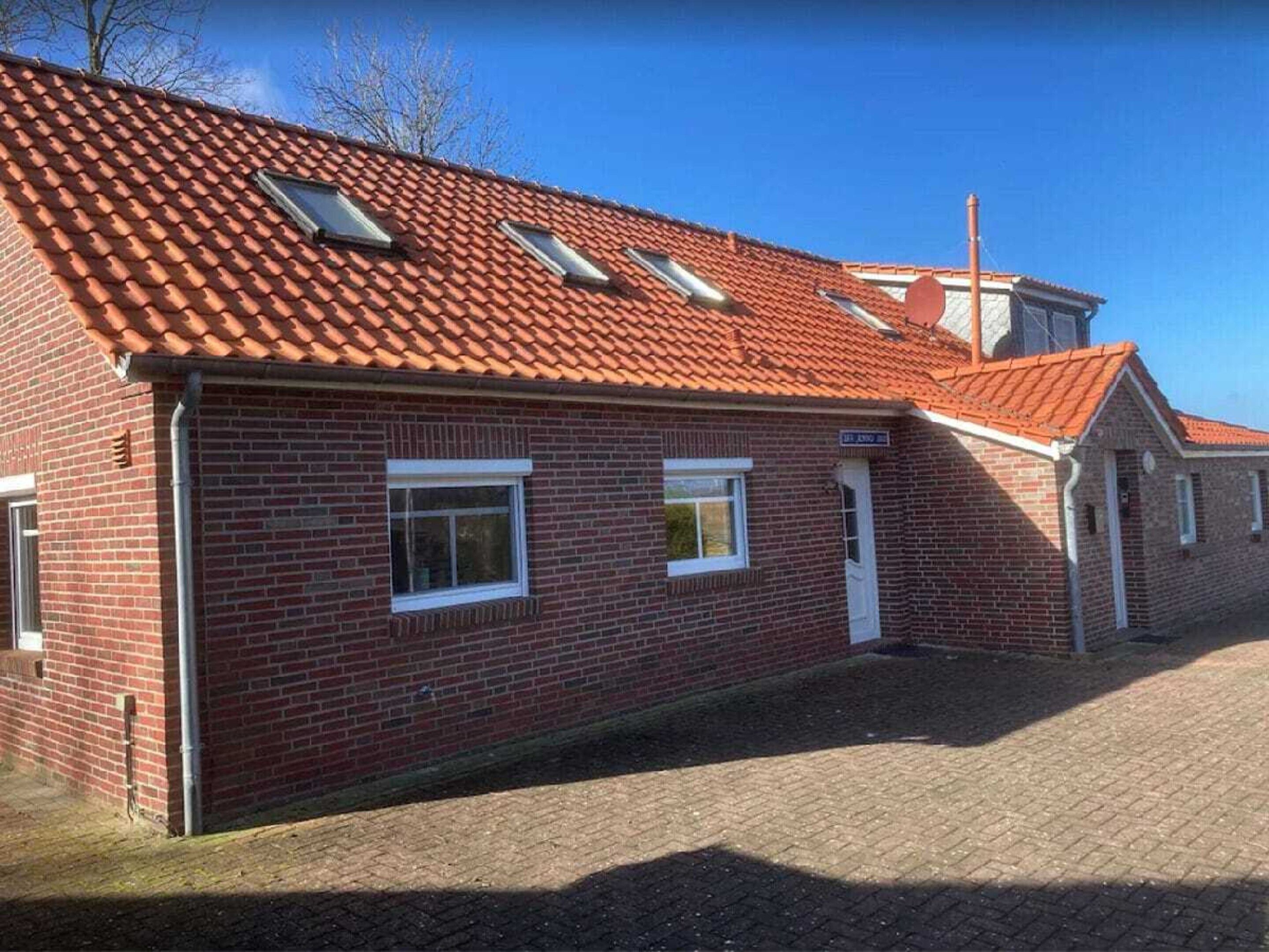 A brick building with a red-tiled roof, two windows, and a door.