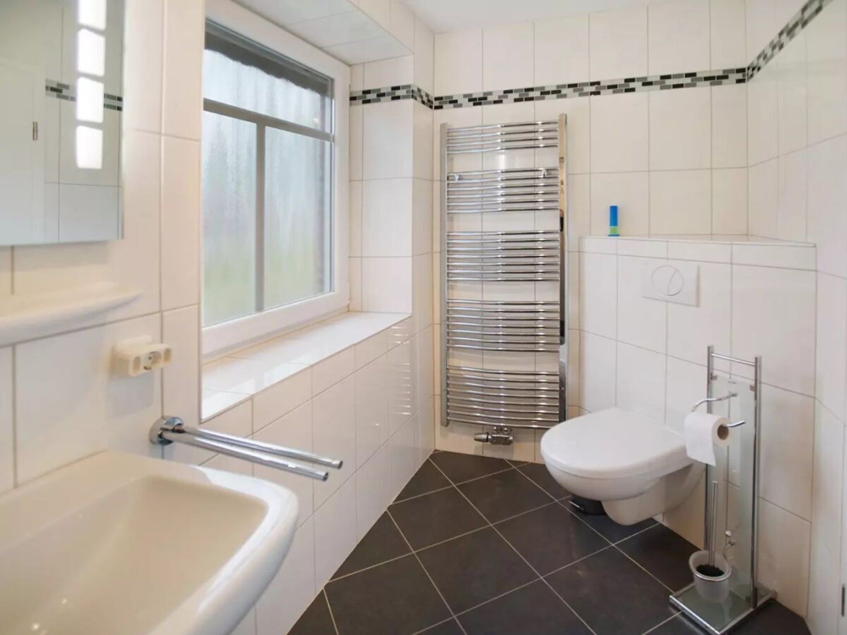 Une salle de bain avec un lavabo blanc, des toilettes, une douche avec une porte en verre et une fenêtre.