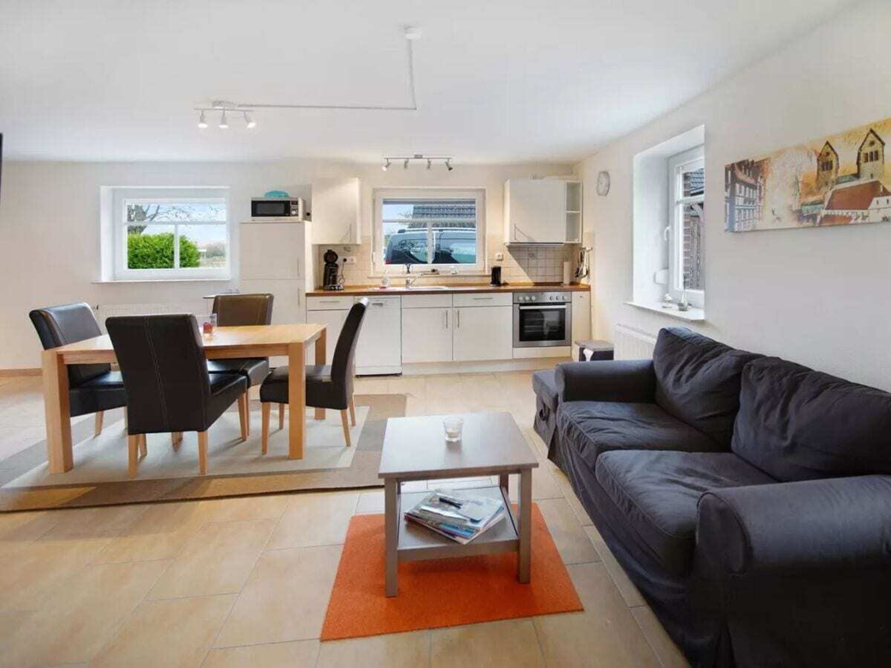 A modern living room with a sofa, a dining table with chairs, a coffee table, and a kitchen area with cabinets and appliances.