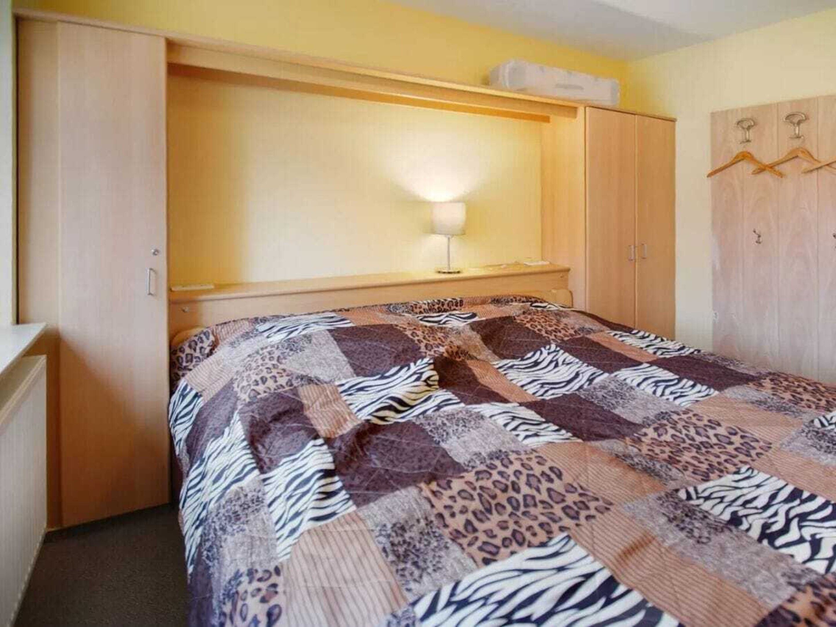 A bedroom with a bed, a bedside lamp, a wardrobe, and a hanging coat rack.