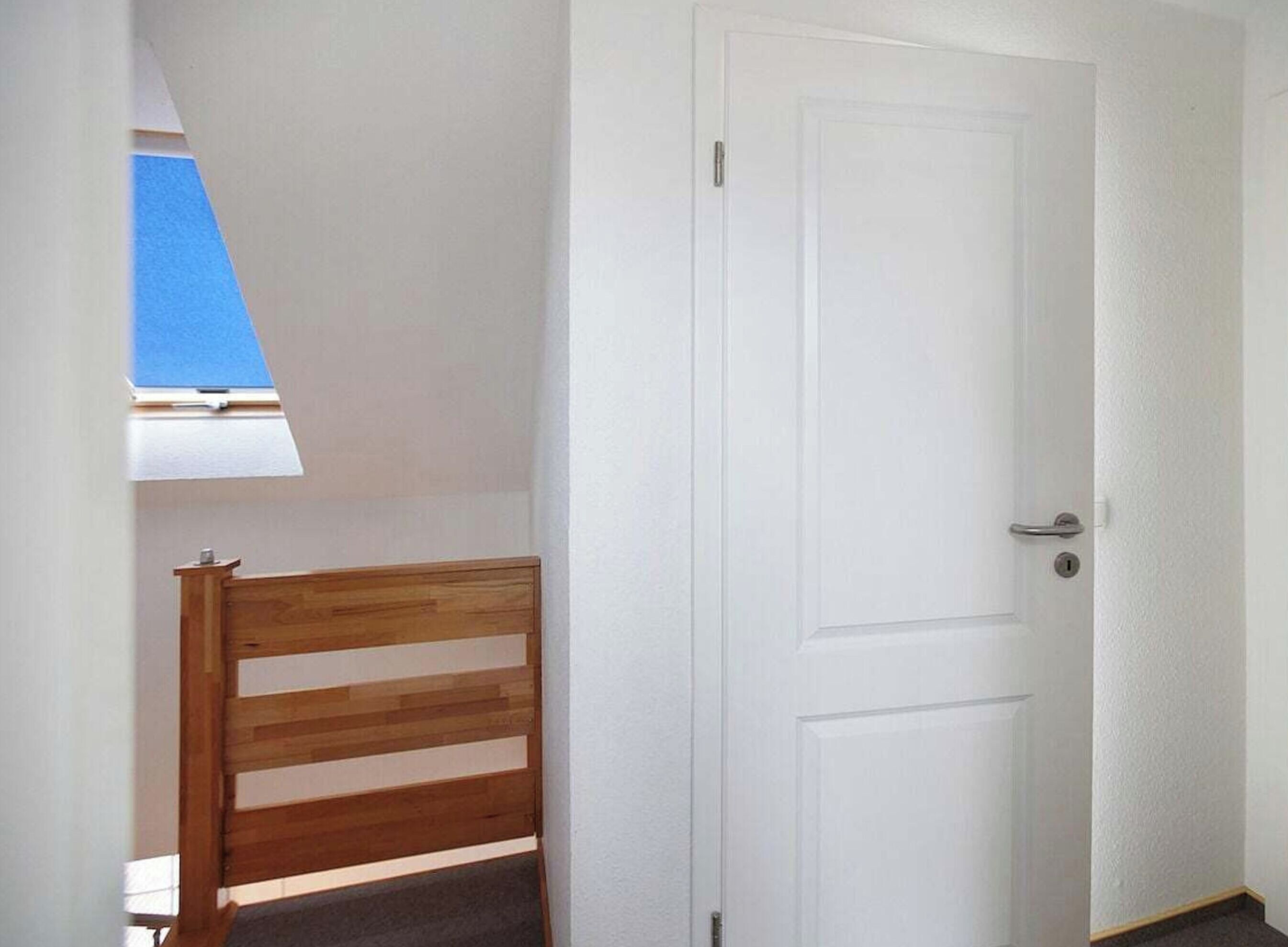 A room with a white door, a wooden chair, and a skylight.