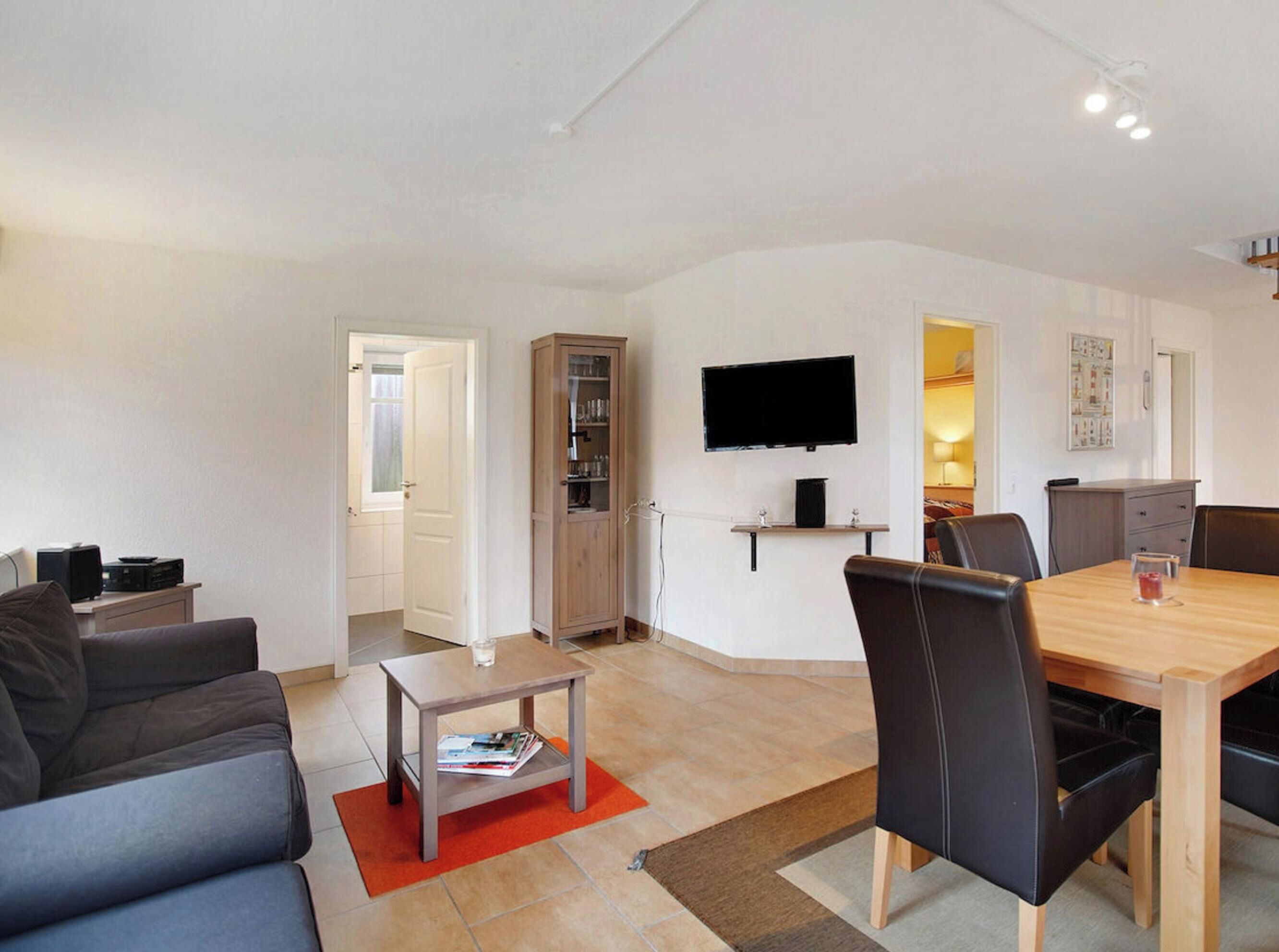 Ein modernes Wohnzimmer mit einer Couch, einem Couchtisch, einem Esstisch mit Stühlen, einem an der Wand befestigten Fernseher und einem Schrank.
