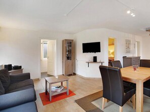 Una sala de estar moderna con un sofá, una mesa de centro, una mesa de comedor con sillas, un televisor montado en la pared y un armario.